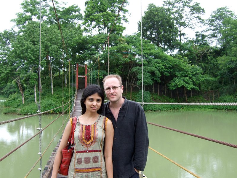 Anika and Chuck on a rope and plank bridge over a lake
