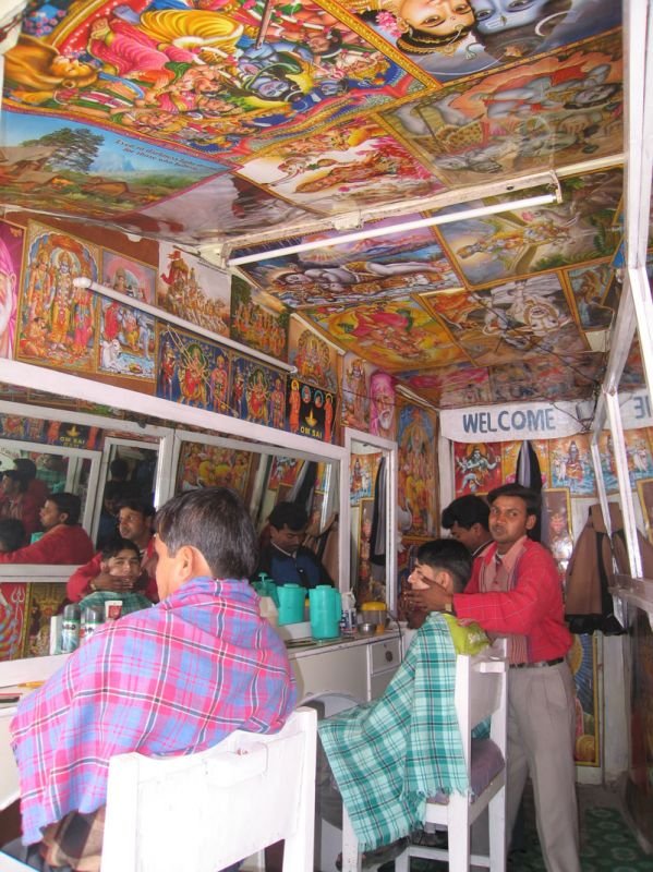 barber shop, every inch covered with posters of hindu gods and goddesses, very colourful
